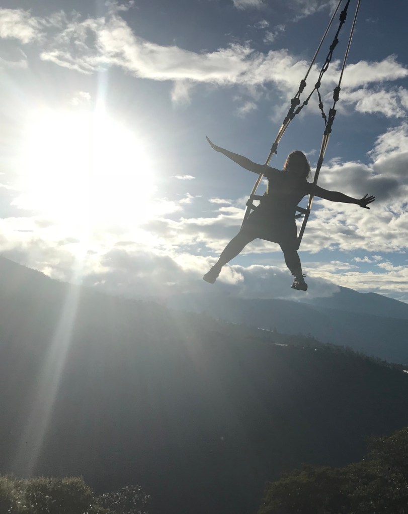 Anna on a swing with her arms and legs spread wide and the sky in the background